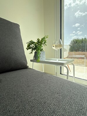 A modern living room with a grey sofa, a small table with a plant and a glass of white wine, and a large window with a view of the outdoors. - Luxury Villa with Private Pool & Stunning Cretan Views Near Heraklion (HERAKLION)