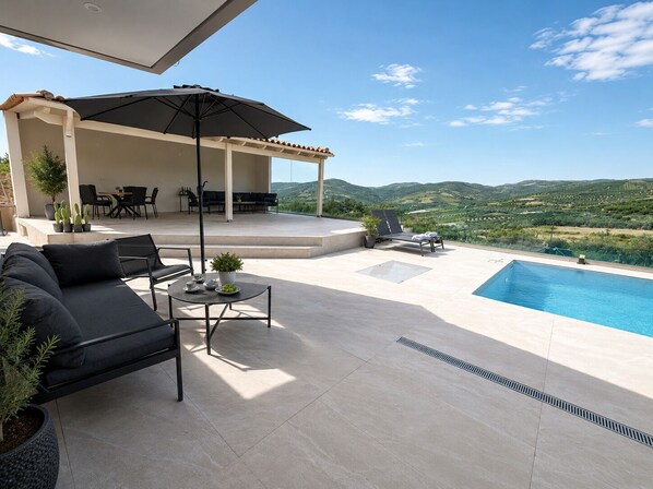 A poolside area with a sofa, chairs, a table, and a covered seating area with a view of the landscape. - Luxury Villa with Private Pool & Stunning Cretan Views Near Heraklion (HERAKLION)