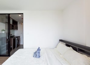 Un dormitorio con cama, una kitchenette pequeña y una puerta de cristal que da a otra habitación.