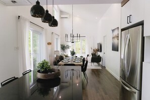 A modern kitchen with a central island, pendant lights, and a stainless steel refrigerator. - Java with Private Spa, Lake & Kayak (St-Raymond)