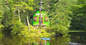 A green cabin with a chimney, surrounded by trees and a body of water. - Java with Private Spa, Lake & Kayak (St-Raymond)