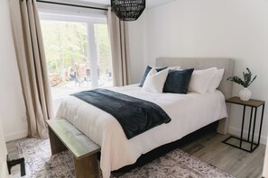 A bedroom with a bed, bench, bedside table, and a view of the outdoors. - Java with Private Spa, Lake & Kayak (St-Raymond)