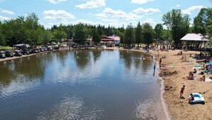 A lake with a sandy beach, surrounded by trees and buildings.