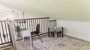 A small, open-plan room with a desk, two chairs, a patterned rug, and a staircase.
