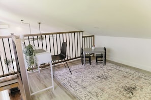 A small, open-plan room with a desk, two chairs, a patterned rug, and a staircase.