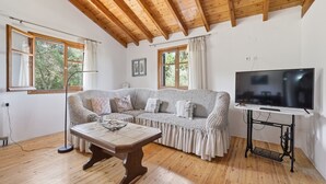 Ett mysigt vardagsrum med ett träpanelat tak, en soffa, ett soffbord, en tv på ett tv-bord och stora fönster.