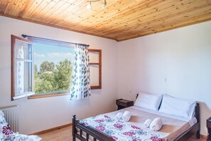 Un dormitorio con techo de madera, un ventanal con vistas y una cama con ropa blanca, junto a una mesita de noche.