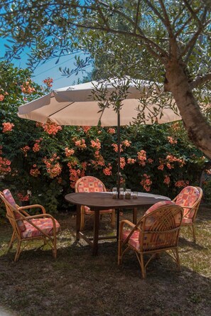An outdoor dining area with a round table, four wicker chairs, and a large umbrella. - Apartment 'Casa Nova Olive Grove' with Sea View, Wi-Fi and Air Conditioning (Lefkimmi)