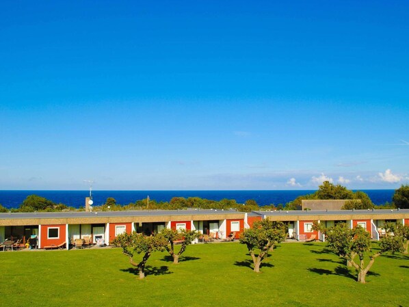 A row of red and white buildings with a grassy lawn in front, overlooking a clear blue sky and ocean. - The Apple Garden (Allinge)