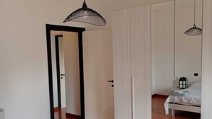 A modern bedroom with a wooden floor, a bed with a white cover, a wardrobe, and a hanging light fixture. - Bright, spacious apartment between Milan and Como. (Lombardia)
