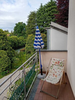 En balkong med ett blårandigt parasoll, ett grönt nät och en stol med ett blommönster.
