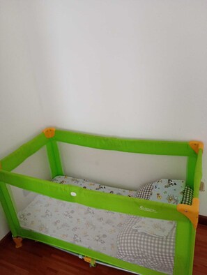 Uma caminha infantil pequena, com estrutura verde e colchão com personagens de desenho animado.
