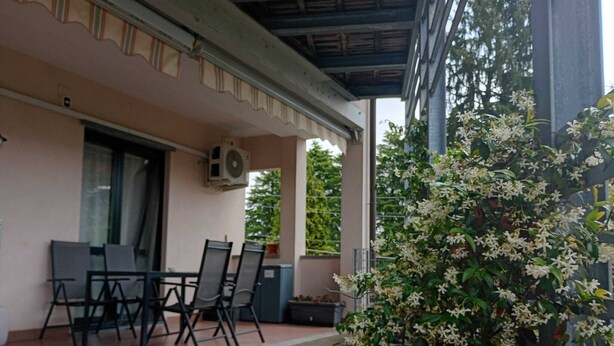 An outdoor patio with a table and chairs, a potted plant, and a building with a tiled roof. - Bright, spacious apartment between Milan and Como. (Lombardia)