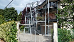 A multi-story building with a metal staircase, a gated entrance, and a garden area. - Bright, spacious apartment between Milan and Como. (Lombardia)
