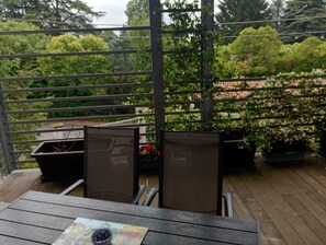 Um deck de madeira com mesa e cadeiras, cercado por uma grade de metal e vegetação.