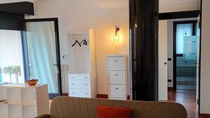 A living room with a sofa, a white cabinet, a black column, and a view of a kitchen. - Bright, spacious apartment between Milan and Como. (Lombardia)