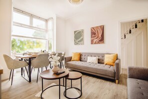 Ein modernes Wohnzimmer mit einem grauen Sofa, einem Esstisch mit Stühlen und einer Treppe.