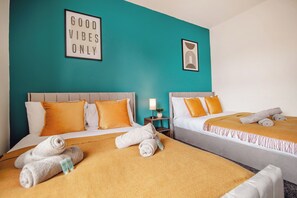 Ein Hotelzimmer mit zwei Betten, jeweils mit Kopfteil, und einer türkis farbenen Akzentwand. Handtücher und ein kleiner Nachttisch mit Lampe sind vorhanden.