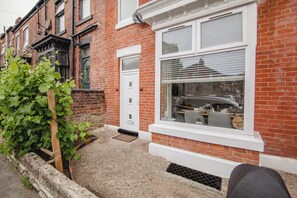 A residential building with a white front door, a window with blinds, and a brick facade. - Group Haven 5 Bed 2 Bath | Hot Tub | Pool Table (Sheffield)