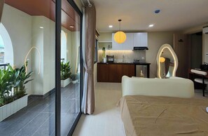 Una habitación de hotel moderna con cama, kitchenette, comedor y un amplio ventanal con cortinas.