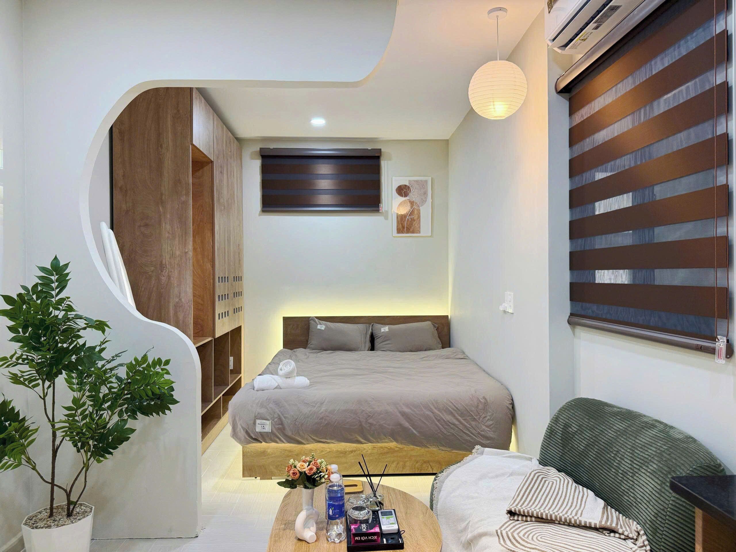 A modern hotel room with a curved wall, a bed, a seating area, and a potted plant.