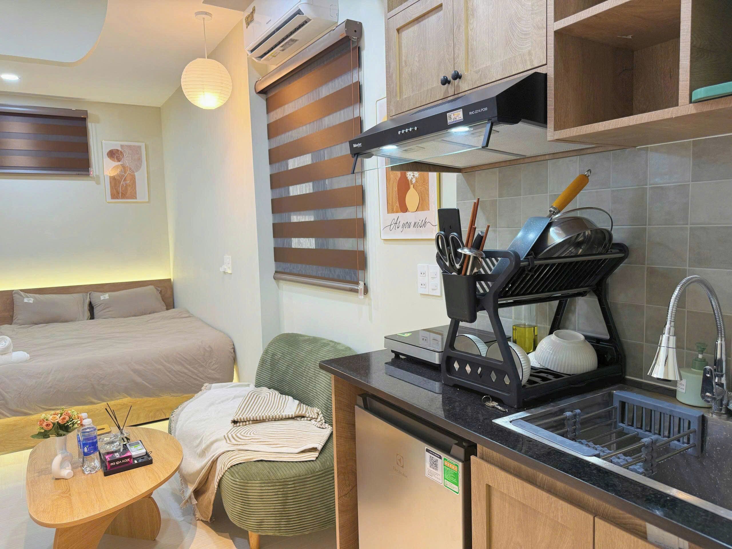 A compact hotel room with a kitchenette, a bed, a small dining table, and a green chair.
