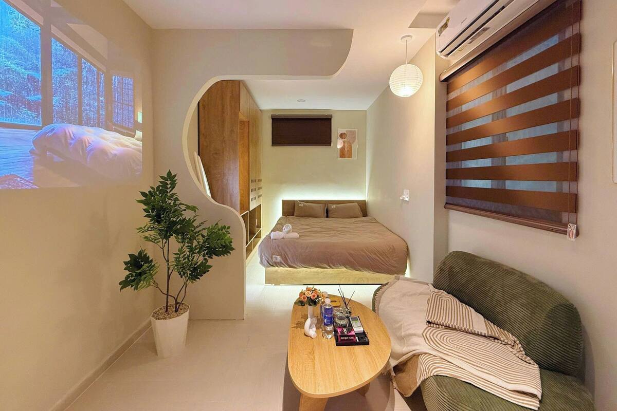 A modern hotel room with a bed, a sofa, a coffee table, and a potted plant.