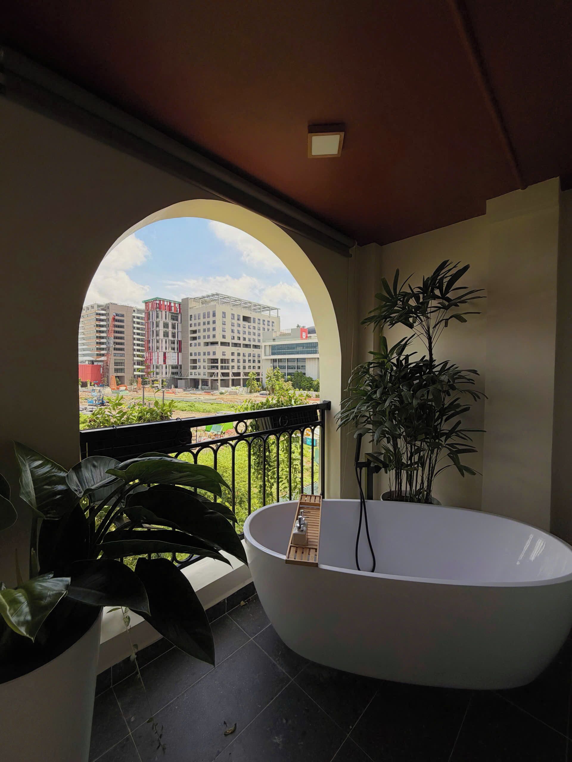 A balcony with a view of buildings, a bathtub, and potted plants.