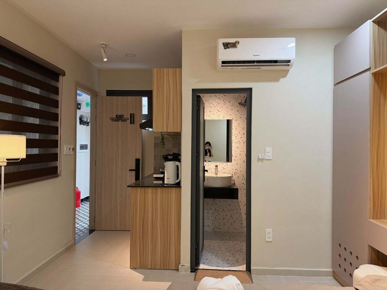 A modern hotel room with a kitchenette, a large mirror, and a ceiling-mounted air conditioner.