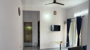 A living room with a flat-screen TV, a ceiling fan, a sofa, a small table, and a door leading to another room.