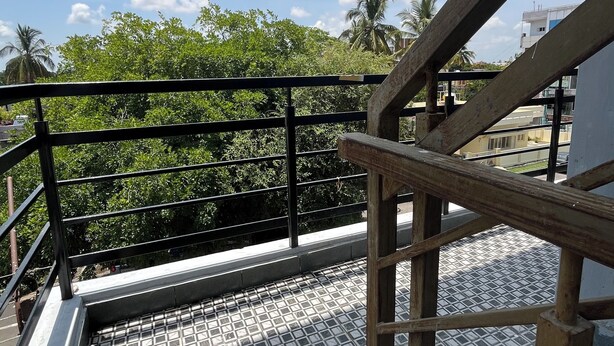 A metal staircase with a metal railing leading to a tiled floor, surrounded by greenery and buildings.