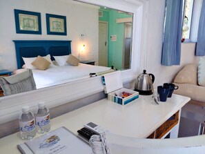 A hotel room with a bed, a desk with a kettle, cups, and a mirror reflecting the room.