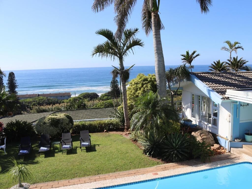 A poolside view with a clear view of the ocean, palm trees, and a house with a tiled roof.