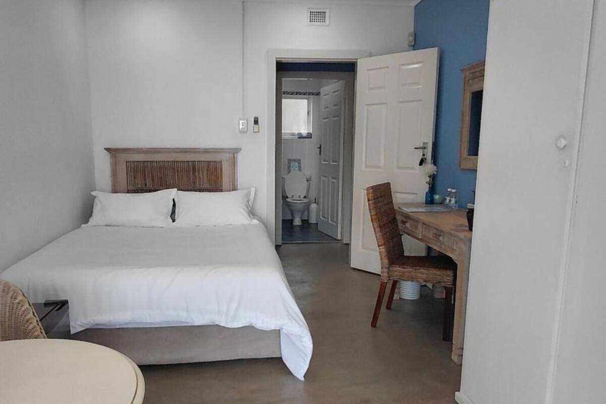 A bedroom with a bed, a desk, and a chair. There is a door leading to a bathroom.
