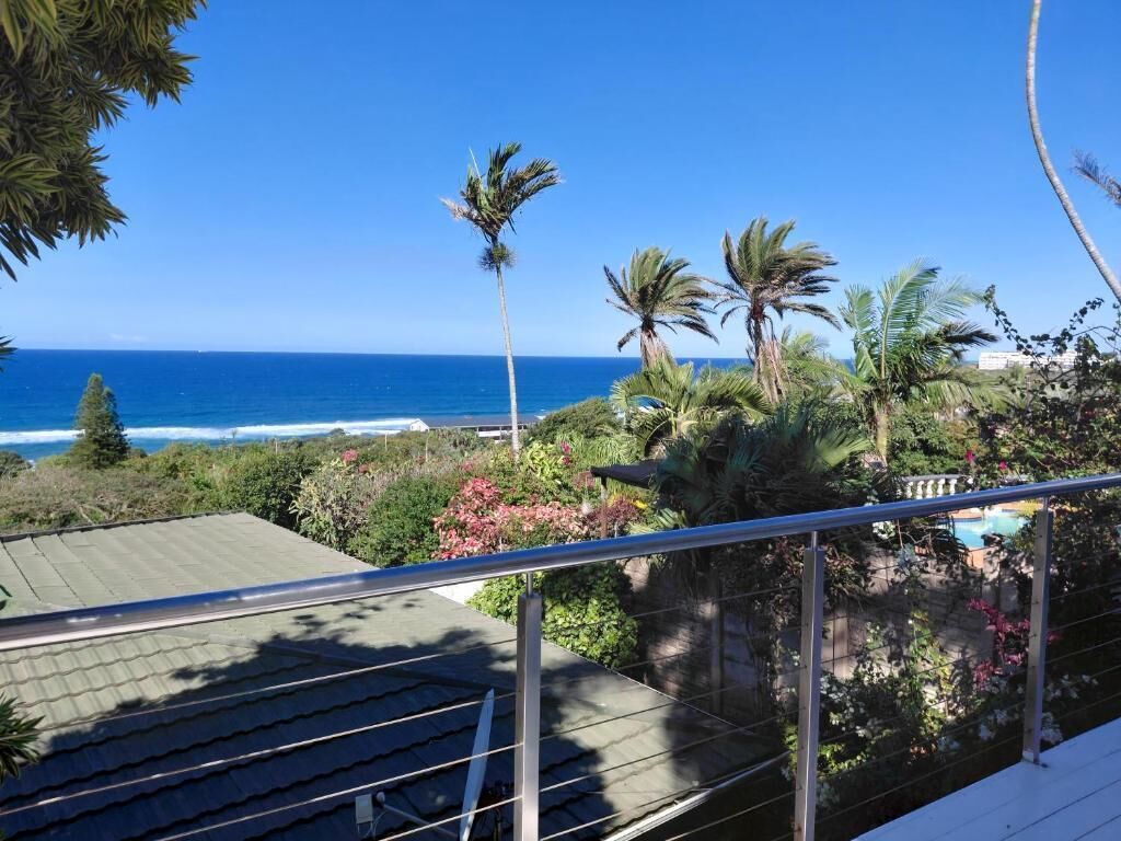 A coastal view with a clear sky, palm trees, and a pool area.