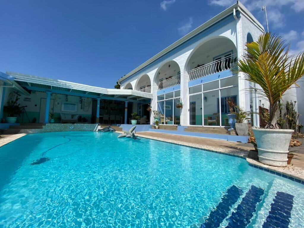 A swimming pool with clear blue water, a covered patio area, and a building with white walls and arches.