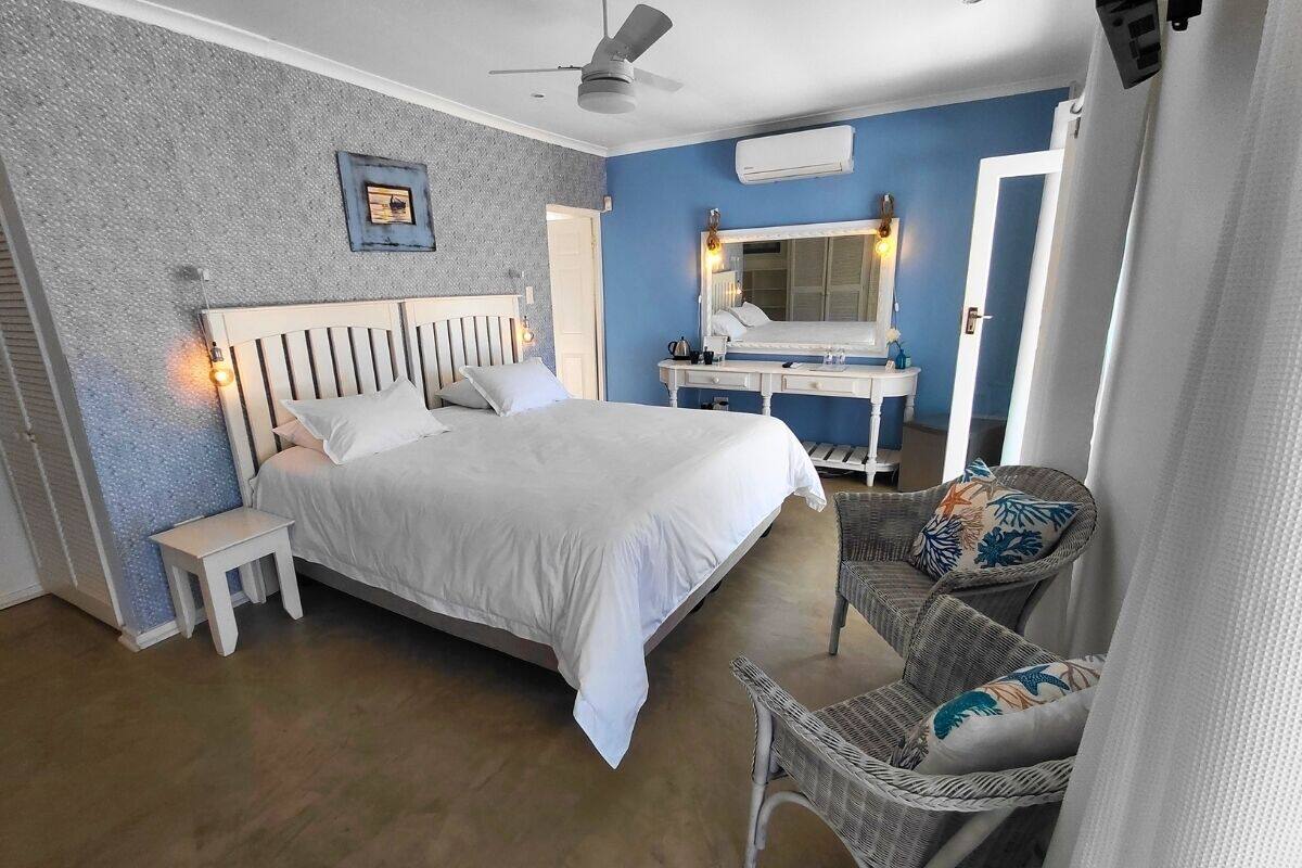 A bedroom with a bed, bedside table, chair, and a mirror.
