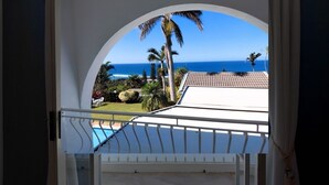 A balcony with a view of the ocean, a swimming pool, and a white building with a tiled roof. - The Lazy Shark (Freeland Park)
