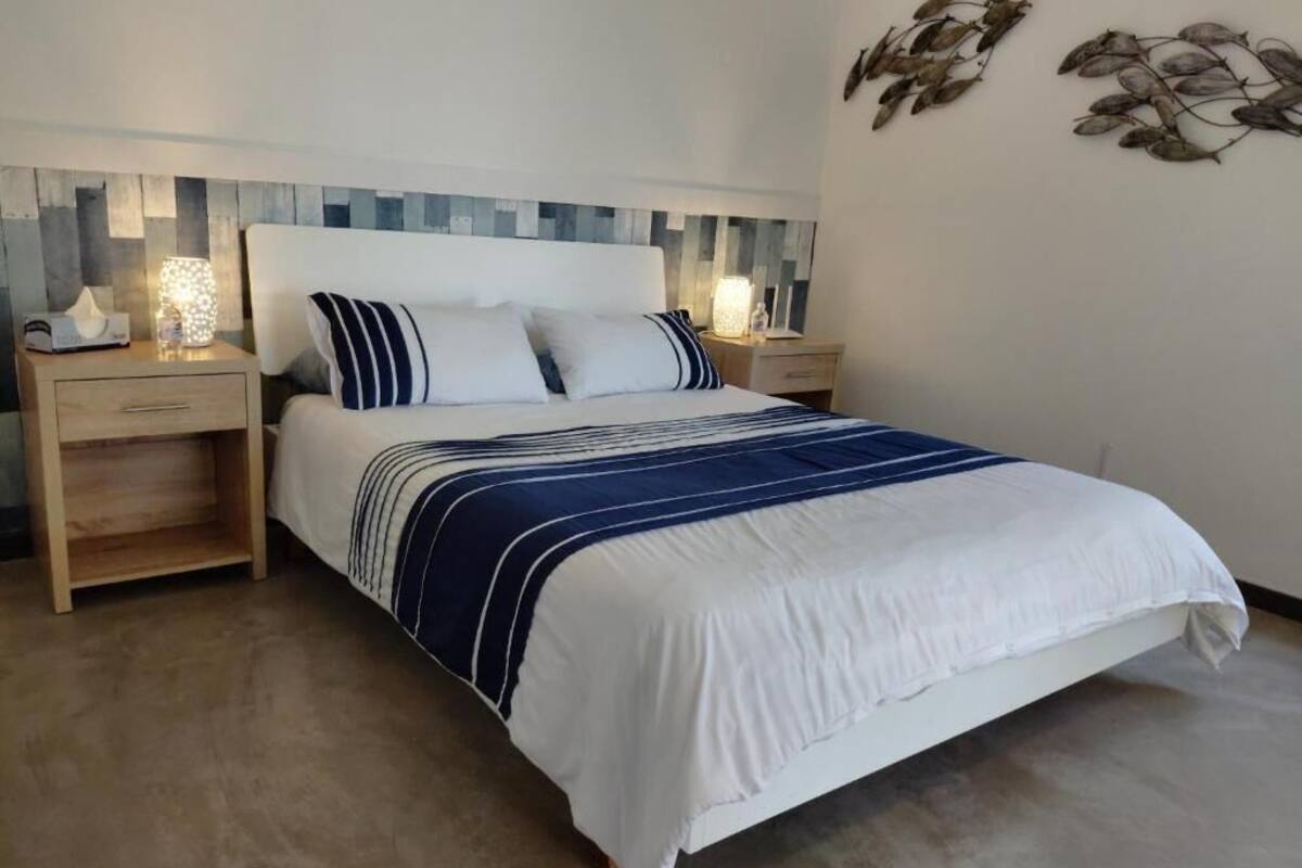A neatly made bed with a striped blanket, wooden nightstands with lamps, and a decorative wall piece.