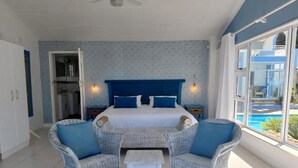 A bedroom with a bed, two wicker chairs, a small table, and a view of a pool. - The Lazy Shark (Freeland Park)