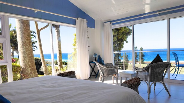 A bedroom with a large bed, a balcony with wicker chairs, and a view of the ocean. - The Lazy Shark (Freeland Park)