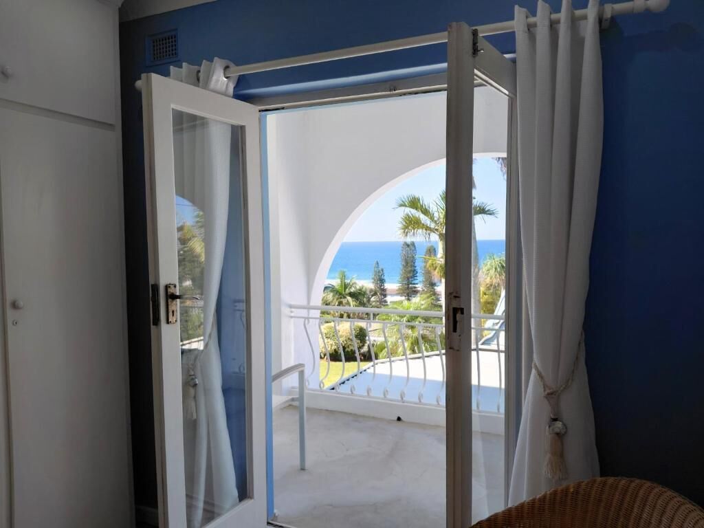 Une chambre avec un balcon, des rideaux blancs et une vue sur la mer.