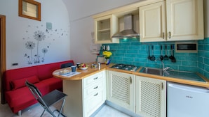 Une cuisine de taille réduite avec un canapé rouge, une petite table à manger, une cuisinière à gaz et un réfrigérateur compact.