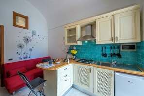 Eine kleine Küche mit einem roten Sofa, einem kleinen Esstisch, einem Gasherd und einem kompakten Kühlschrank.
