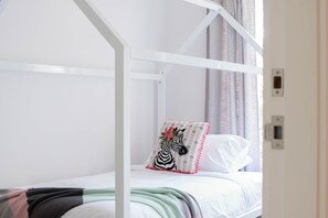 A white bunk bed with a zebra-patterned pillow and a plain pillow, a knitted blanket, and a window with curtains. - “Surfer's Abode” – minutes to the Beach (Avoca Beach)