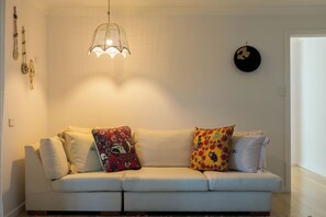 A white sofa with colorful pillows, a hanging light fixture, and wall decorations. - “Surfer's Abode” – minutes to the Beach (Avoca Beach)