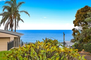 Eine Küstenansicht mit Palmen, wolkenlosem Himmel und einem Gebäude mit Balkon mit Blick auf das Meer.