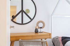 Ein Zimmer mit einem Holztisch, einer Friedenssymbol-Dekoration, einer kleinen Figur und einem Korbstuhl.