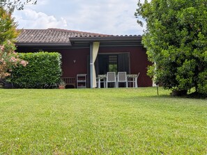 A house with a red exterior, a covered patio with a table and chairs, and a well-maintained lawn.