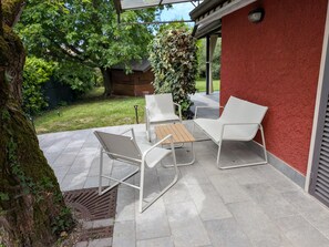 A patio with white chairs and a table, a red wall, and a tree with moss. - Villa Lucrezia – 4 guests in Bardolino, Lake Garda – Pool, Garden, Parking, Pets Welcome (Bardolino)